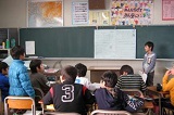 黒板の前で紙を広げて発表している生徒の写真