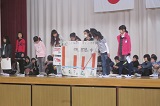 舞台の上で紙を広げている生徒達の写真