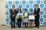 市長と表彰状を持った子ども、認定証をもったこども、市長、教諭2名(向山小)