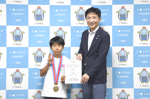 来訪者と市長が、賞状とメダルを手に記念撮影した写真