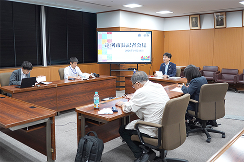 定例市長記者会見に集まった記者と市長の写真